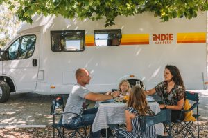 Eine Familie sitzt vor einem Wohnmobil und frühstückt gemeinsam