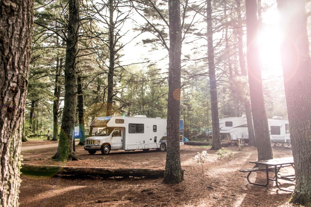 Camper tussen de bomen en een mooie velle zon in de achtergrond