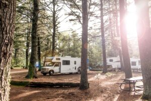 Camper tussen de bomen en een mooie velle zon in de achtergrond