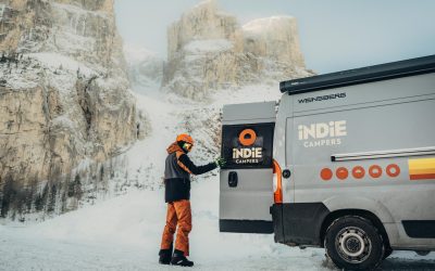 A motorhome parked beside a snow covered mountain road at sunrise, with visible snow chains on its tires and light snow falling, cozy yet adventurous moo