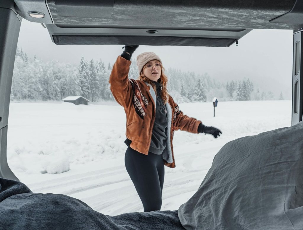 Van aménagé garé dans un paysage hivernal, avec de la neige autour et de la vapeur sortant du chauffage, illustrant un voyage en camping-car en hiver.