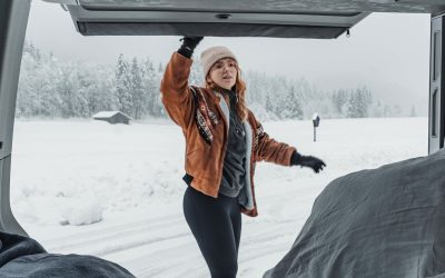 Van aménagé garé dans un paysage hivernal, avec de la neige autour et de la vapeur sortant du chauffage, illustrant un voyage en camping-car en hiver.