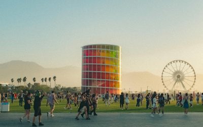 Crowds enjoying a sunset performance at Coachella Festival, with palm trees, art installations, and the Ferris wheel in the background.