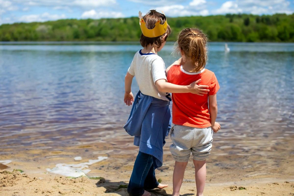 Two young children standing together at the edge of a lake