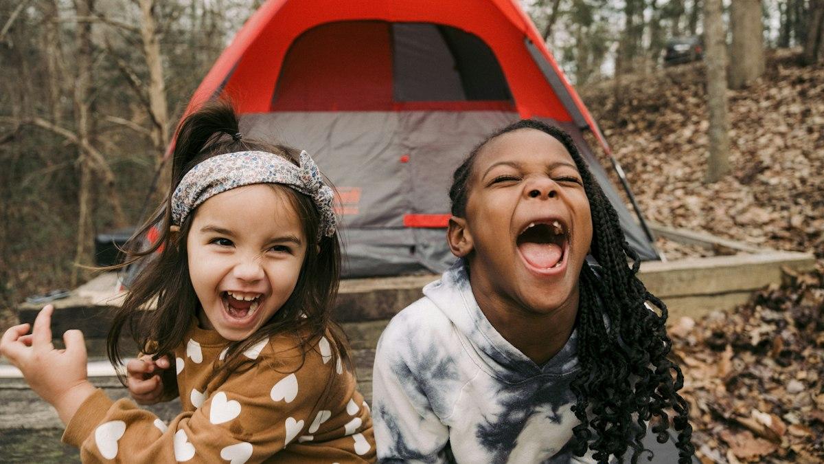 Two laughing girls at a campsite in front of a tent