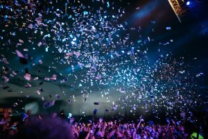 Festival crowd celebrating under falling confetti and stage lights